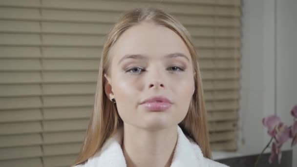 Porträt einer attraktiven lächelnden blonden Frau. im weißen Bademantel nach dem Eingriff. Kosmetologie und Wellness-Center-Konzept. — Stockvideo