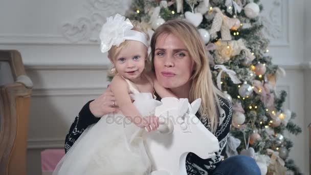 Gelukkig moeder en dochter omarmen. Witte muur en versierde boom op achtergrond. Kerstmis of Nieuwjaar viering. — Stockvideo
