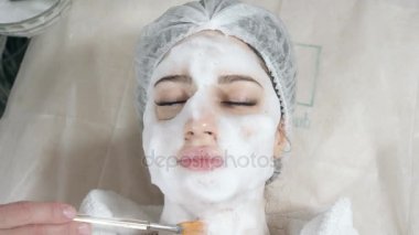 Genç güzel kadın güzellik salonları içinde tedavi alma. Genç güzel esmer kadını kanepede yatan office güzellik uzmanı. Yüz temizleyici köpük kullanarak.