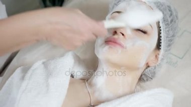 Genç güzel kadın güzellik salonları içinde tedavi alma. Genç güzel esmer kadını kanepede yatan office güzellik uzmanı. Yüz temizleyici köpük kullanarak.