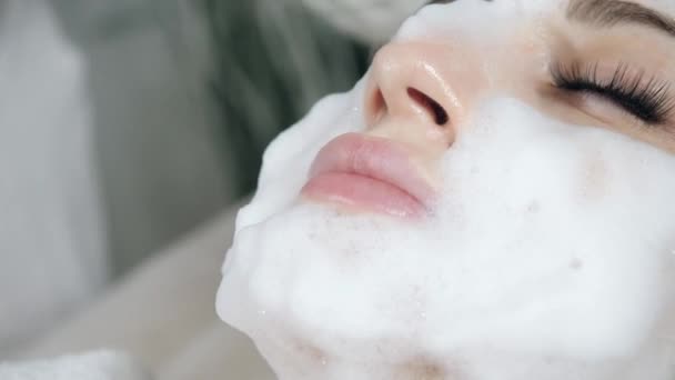 Mujer bonita joven recibiendo tratamientos en salones de belleza. Joven hermosa mujer morena en la oficina esteticista acostado en el sofá. Espuma de limpieza facial usando . — Vídeos de Stock