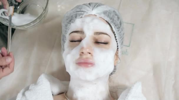 Mujer bonita joven recibiendo tratamientos en salones de belleza. Joven hermosa mujer morena en la oficina esteticista acostado en el sofá. Espuma de limpieza facial usando . — Vídeos de Stock