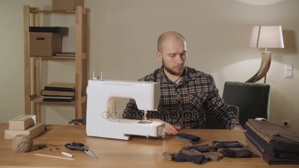 Νεαρός άνδρας βγάζει ένα κουτί με κλωστές και βελόνες. Εργάζεται ως έναν Ράφτη και χρησιμοποιώντας μια ράβοντας μηχανή σε ένα στούντιο κλωστοϋφαντουργίας. παπιγιόν από μάλλινα. — Αρχείο Βίντεο