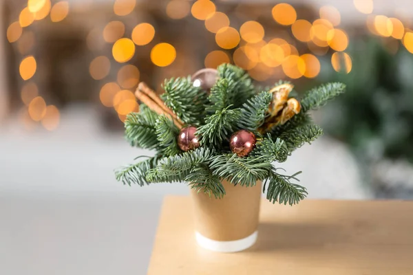 Ambachtelijke papier koffie kopjes op een houten tafel. Het concept van kerst koffie met decoraties fir tree. Op de achtergrond bokeh gloeilamp krans — Stockfoto