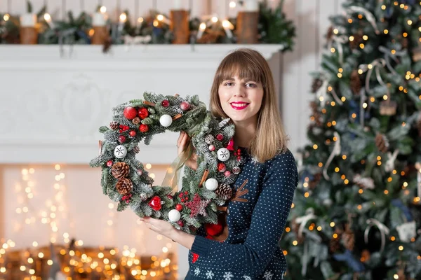 젊은 여자는 휴가 대 한 전나무와 크리스마스 화 환을 들고. 새 해 축 하입니다. 벽난로 크리스마스 트리, 조명, 배경 화 — 스톡 사진