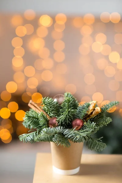 Ambachtelijke papier koffie kopjes op een houten tafel. Het concept van kerst koffie met decoraties fir tree. Op de achtergrond bokeh gloeilamp krans — Stockfoto