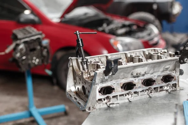 Enfoque selectivo. Bloque del motor en un soporte de reparación con pistón y varilla de conexión de la tecnología automotriz. Coche rojo borroso en el fondo. Interior de un taller de reparación de automóviles . — Foto de Stock