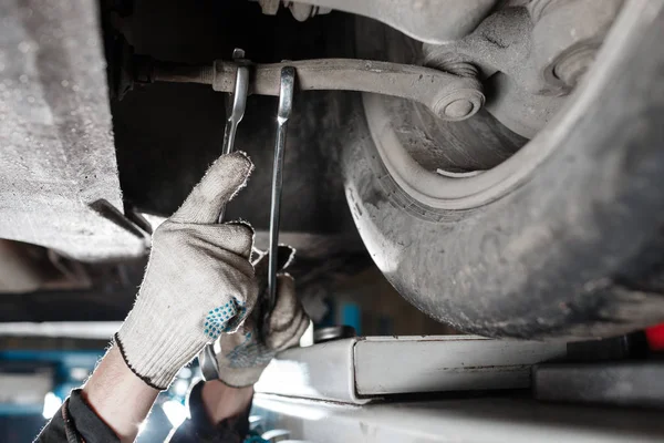 Araba tamircisi tamir istasyonunda kaldırılan otomobilin süspansiyonunu inceliyor.
