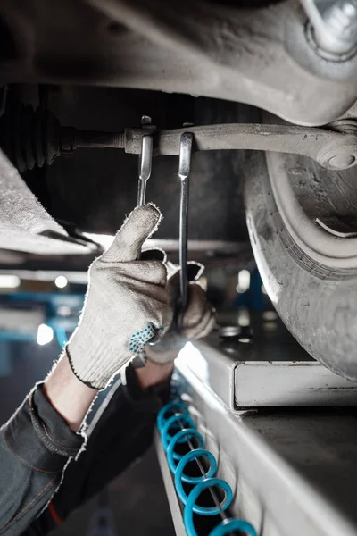 Araba tamircisi tamir istasyonunda kaldırılan otomobilin süspansiyonunu inceliyor.