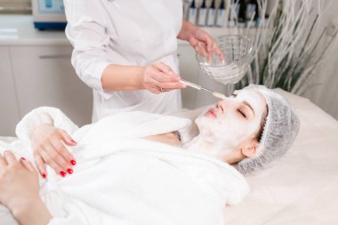 Genç güzel kadın güzellik salonları içinde tedavi alma. Genç güzel esmer kadını kanepede yatan office güzellik uzmanı. Yüz temizleyici köpük kullanarak.