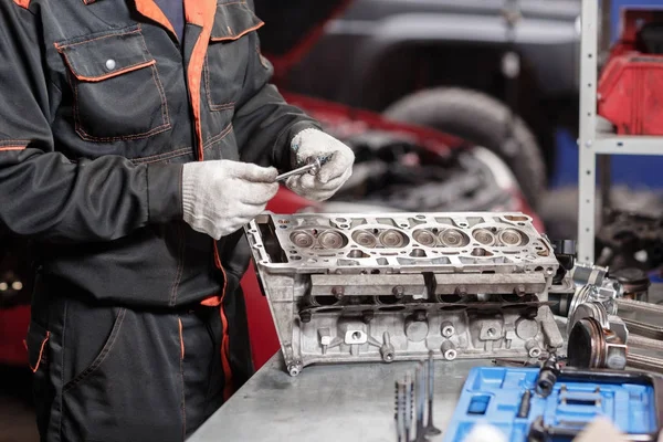 Enfoque selectivo. Bloque del motor en un soporte de reparación con pistón y varilla de conexión de la tecnología automotriz. Coche rojo borroso en el fondo. Interior de un taller de reparación de automóviles . — Foto de Stock