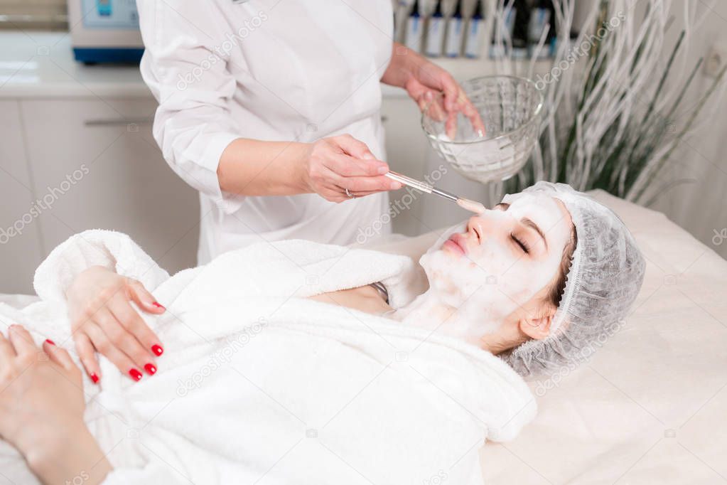 Young pretty woman receiving treatments in beauty salons. Young beautiful dark-haired woman in the office beautician lying on the couch. Facial cleansing foam using.