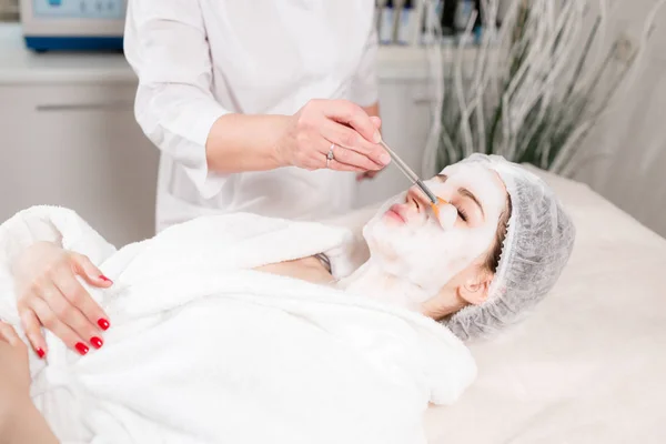 Jovem mulher bonita recebendo tratamentos em salões de beleza. Jovem bela mulher de cabelos escuros no escritório esteticista deitado no sofá. Espuma de limpeza facial usando . — Fotografia de Stock