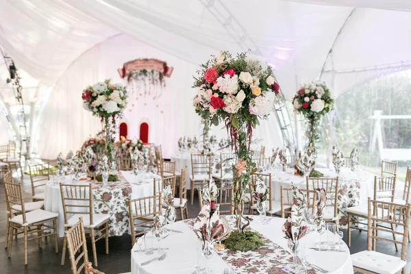 Interior of a wedding tent decoration ready for guests. Served round banquet table outdoor in marquee decorated flowers and silk. Catering concept