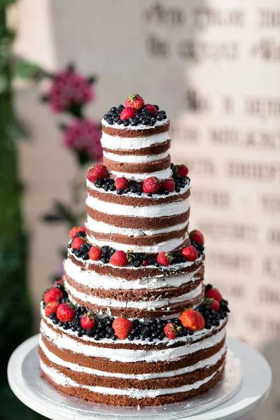 Round multi tiered wedding cake with sponge, cream, jam and berries on a circular base. Fresh blueberries and strawberries