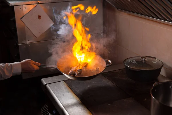 Flambe lamb rib roast. Cooking with fire in frying pan. Professional chef in a commercial kitchen cooking. Man frying food in flaming pan on hob in outdoor kitchen. slow motion