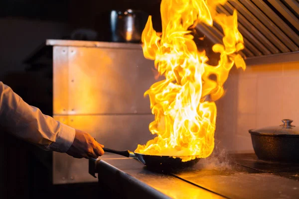 Flambe lamb rib roast. Cooking with fire in frying pan. Professional chef in a commercial kitchen cooking. Man frying food in flaming pan on hob in outdoor kitchen. slow motion