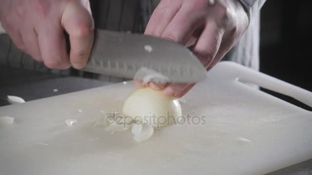 Primer plano de la mano con cuchillo de corte vegetal fresco. Joven chef cortando cebolla en un primer plano de tabla de cortar blanco. Cocinar en una cocina de restaurante — Vídeo de stock