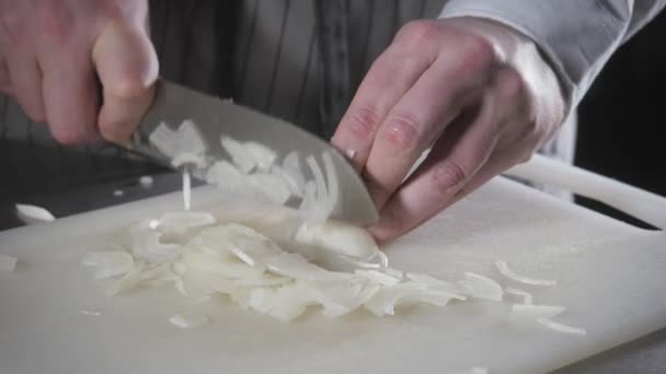 Primo piano di mano con coltello che taglia verdura fresca. Giovane chef taglio cipolla su un tagliere bianco primo piano. Cucinare in una cucina ristorante — Video Stock