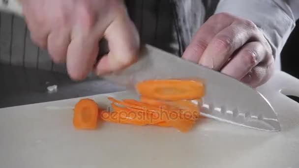 Primer plano de la mano con cuchillo de corte vegetal fresco. Joven chef cortando zanahorias en un primer plano de tabla de cortar blanco. Cocinar en una cocina de restaurante — Vídeos de Stock