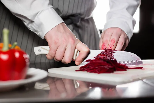 Крупный план руки с ножом, обрезающим свежий овощ. Молодой шеф-повар режет свеклу на белой доске крупным планом. Кулинария на кухне ресторана — стоковое фото