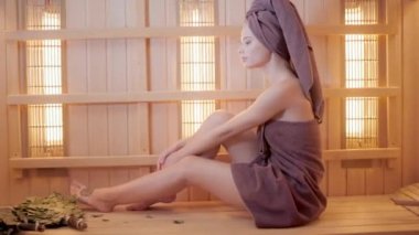 Genç kadın bir saunada dinlendirici bir havlu ile giyinmiş. Yeni Fin saunası, tıbbi prosedürler, Klasik Ahşap sauna için kızılötesi paneller iç.