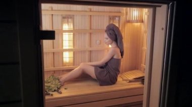 Genç kadın bir saunada dinlendirici bir havlu ile giyinmiş. Yeni Fin saunası, tıbbi prosedürler, Klasik Ahşap sauna için kızılötesi paneller iç.