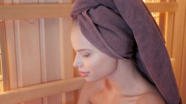 Młoda kobieta na relaks w saunie, ubrany w ręcznik. Wnętrze Nowa sauna fińska, podczerwień panele do procedur medycznych, klasycznej sauny drewniane. — Wideo stockowe