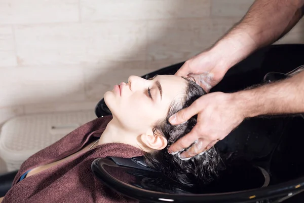 beautiful girl washes her hair before a haircut in a beauty salon. hair washing at a hairdressing, young caucasian girl. professional shampoo. stylist hairdresser man