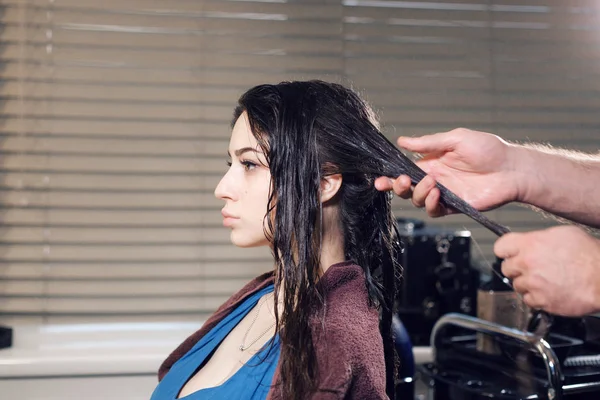 Closeup hairdresser man makes hairstyle for young woman in beauty salon