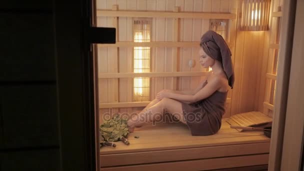 Jeune femme se relaxant dans un sauna habillé d'une serviette. Intérieur du nouveau sauna finlandais, panneaux infrarouges pour les procédures médicales, sauna en bois classique . — Video