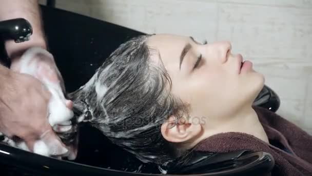 Menina bonita lava o cabelo antes de um corte de cabelo em um salão de beleza. lavagem de cabelo em um cabeleireiro, menina caucasiana jovem. champô profissional. cabeleireiro estilista homem — Vídeo de Stock