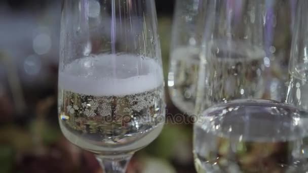 Ο σερβιτόρος εκβάλλει τα ποτήρια της σαμπάνιας. Πίνακας κορυφή γεμάτο ποτήρια αφρώδες λευκό κρασί με φιάλες στο παρασκήνιο. — Αρχείο Βίντεο