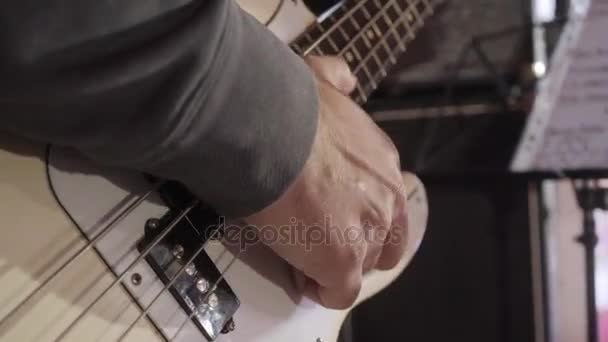Закрыть на пальцах молодого человека, играющего на бас-гитаре на сцене — стоковое видео