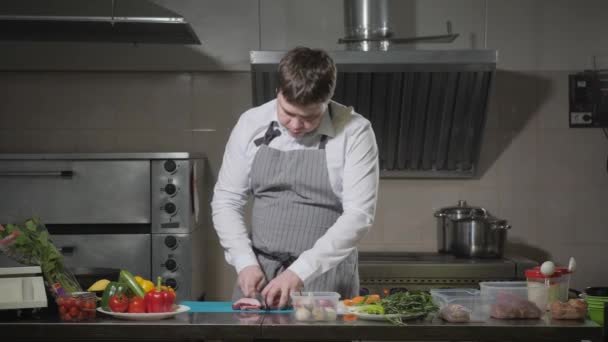 Joven chef cortando pimentón en un primer plano de tabla de cortar blanco. Cocinar en una cocina de restaurante — Vídeo de stock