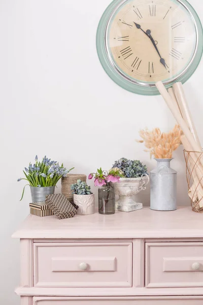 Ανοιξιάτικη διάθεση. Vintage διακόσμηση. ροζ παστέλ ντουλάπα. Ξηρό anf φρέσκα λουλούδια στο ξύλινο τραπέζι. Ένα μεγάλο ρολόι σε ένα λευκό τοίχο. χώρο αντίγραφο — Φωτογραφία Αρχείου