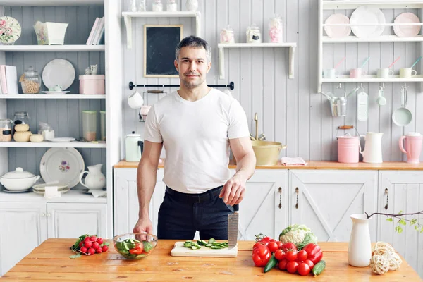 Porträtt av stilig leende man på kök. matlagning och hem koncept - Närbild manlig hand hugga gurka på skärbräda med vass kniv — Stockfoto