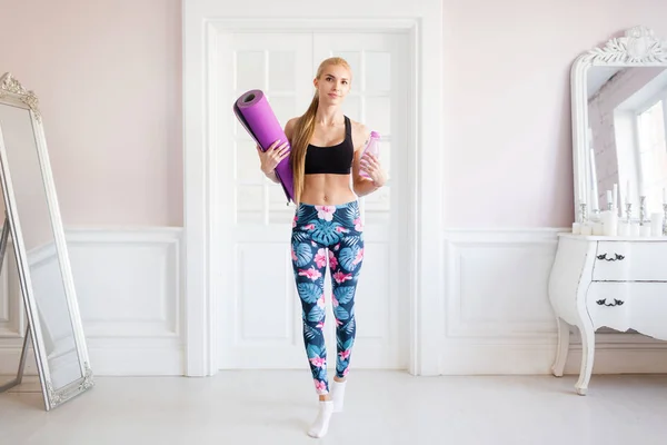 home fitness. Portrait young sports woman. With fitness Mat and clean water a bottle.
