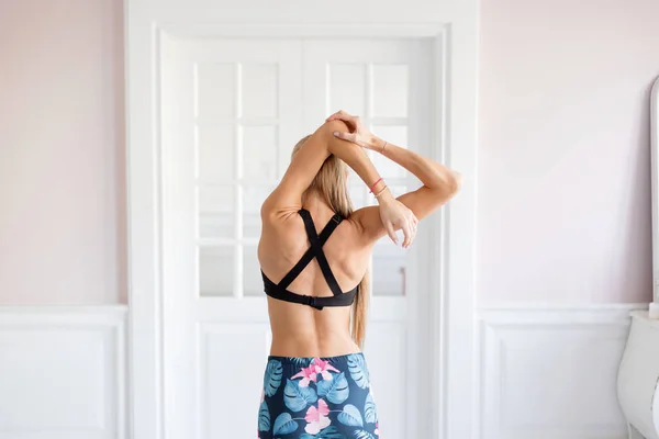 Home fitness. Young woman warming up before training doing exercises to stretch her muscles and joints. Lovely young blonde girl — Stock Photo, Image