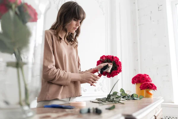 Ung kvinna florist arrangera växter i blomsteraffär. Människor, företag, försäljning och blomsterhandel koncept. Bukett med röda rosor — Stockfoto