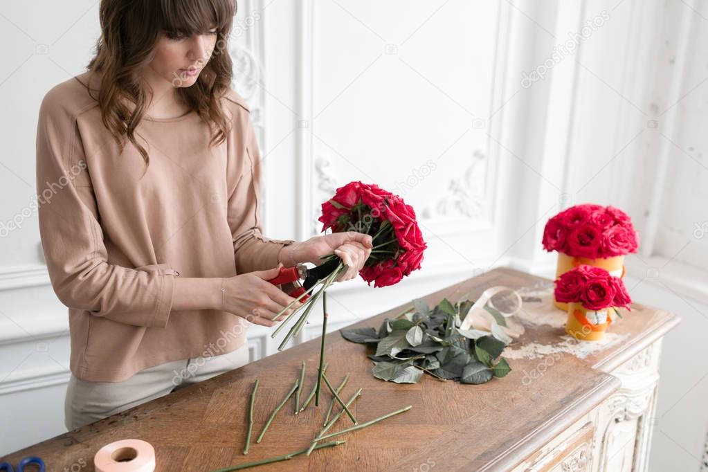 Young woman florist arranging plants in flower shop. People, business, sale and floristry concept. Bouquet of red roses