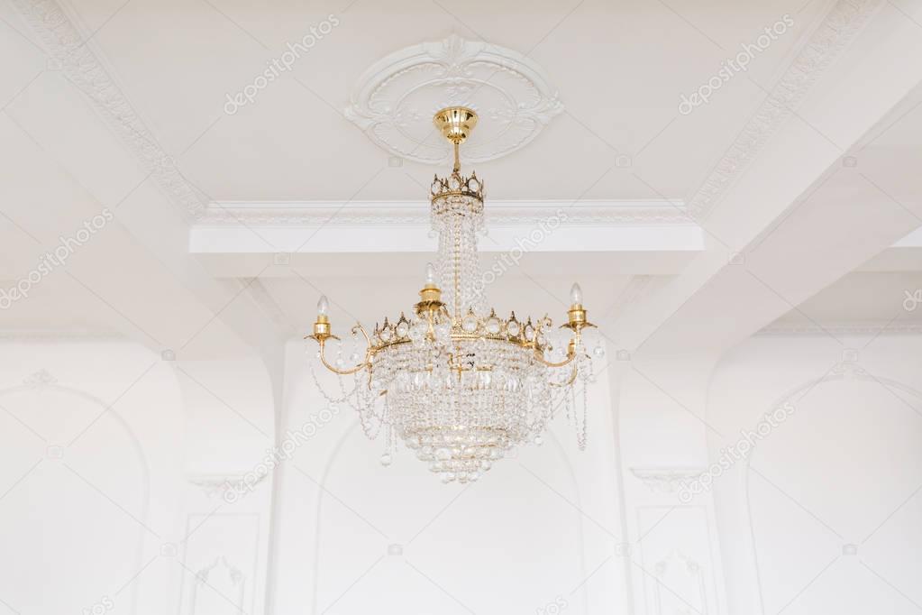 Expensive interior. Large electric chandelier made of transparent glass beads. White ceiling decorated with stucco molding. White patterned. Mouldings element from gypsum.