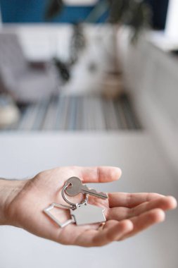 Ev şekilli anahtarlığı olan adamlar el ele tutuşuyorlar. Modern ışık lobisi. İpotek konsepti. Gayrimenkul, taşınma ya da ev kiralama.