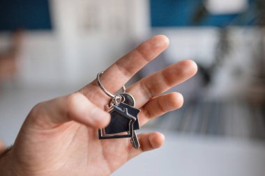 Ev şekilli anahtarlığı olan adamlar el ele tutuşuyorlar. Modern ışık lobisi. İpotek konsepti. Gayrimenkul, taşınma ya da ev kiralama.