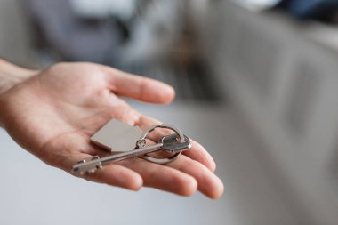 Ev şekilli anahtarlığı olan adamlar el ele tutuşuyorlar. Modern ışık lobisi. İpotek konsepti. Gayrimenkul, taşınma ya da ev kiralama.