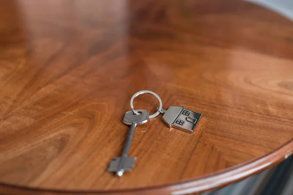 房子钥匙和钥匙串以房子的形式在木桌。不动产、抵押、搬家或租赁财产的概念. — 图库照片