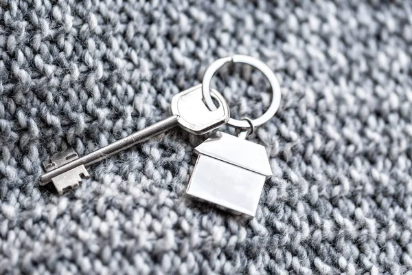 La llave de la casa y el llavero en forma de hogares se encuentra en la tela de lana de punto. Concepto de bienes raíces, hipoteca, mudanza o alquiler de propiedades . — Foto de Stock