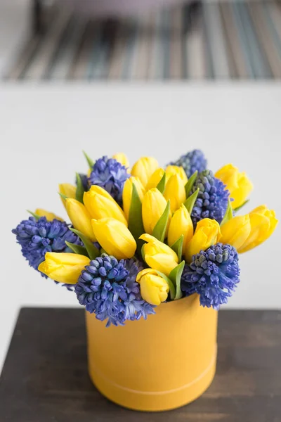 Sunny spring morning. Bunch of blue hyacinths and yellow tulips on wooden table. Present for a girl. Flowers bouquet in box