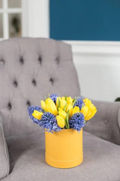 Sunny spring morning. Flowers bouquet in box. Bunch of blue hyacinths and yellow tulips on gray armchair . Present for a girl.