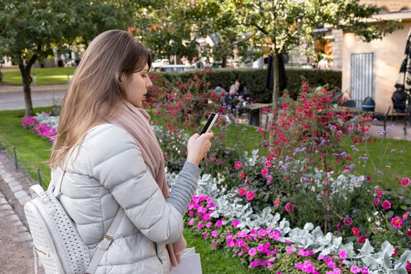Young girl messaging smart phone on the park. in warm clothes. looking at phone — Stock Photo, Image